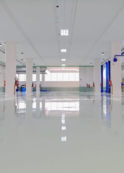 A spacious, clean automotive workshop with empty work bays, blue vehicle lifts, and polished floors. Fire extinguishers are mounted on white columns, while shelves display EPON 1001F and premium release agents.