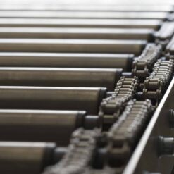 Close-up of a metal roller conveyor system featuring cylindrical rollers and chain mechanisms, efficiently moving items with the help of discontinued Teflon™ White Lithium Grease for smooth operation.