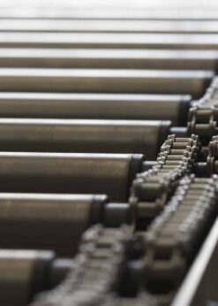 Close-up of a metal roller conveyor system featuring cylindrical rollers and chain mechanisms, efficiently moving items with the help of discontinued Teflon™ White Lithium Grease for smooth operation.