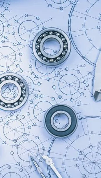 Mechanical bearings placed on engineering blueprints with circular designs and measurement markings.