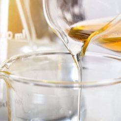 A clear liquid being poured from a glass beaker into another glass container.