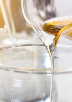 A clear liquid being poured from a glass beaker into another glass container.